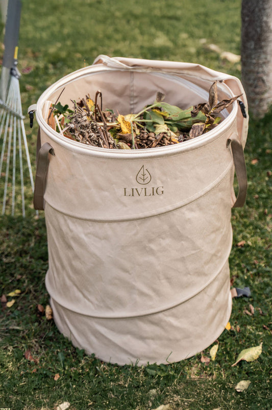 Beiger LIVLIG Pop-up Gartensack mit 90 Litern Fassungsvermögen steht im Garten auf dem Rasen und ist bereits mit Gartenabfällen, Laub und verwelkten Pflanzenresten gefüllt. Der stabile, faltbare Laubsack aus strapazierfähigem Oxford-Gewebe bleibt durch die Pop-up-Funktion von selbst aufrecht stehen und eignet sich ideal als robuster Gartenabfallsack.
