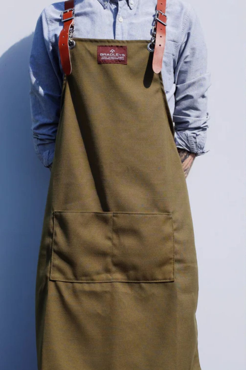 Khakifarbene Gartenschürze mit Lederriemen getragen, robuste Baumwollschürze für Gartenarbeit.