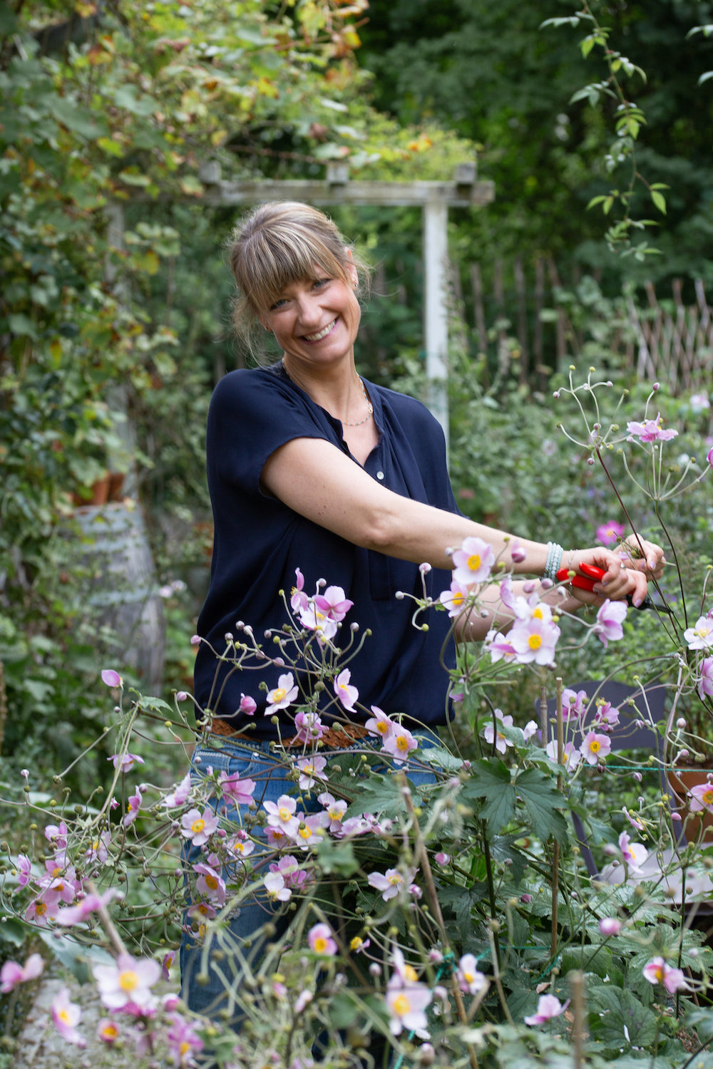 Eine Frau im Garten vor ihr Herbstanemonen. 