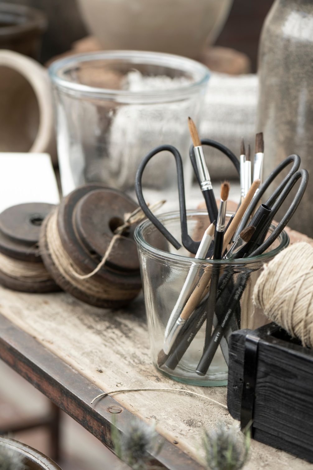 Große Metallschere in einem Glas mit Stiften und Kordel auf Holztisch.